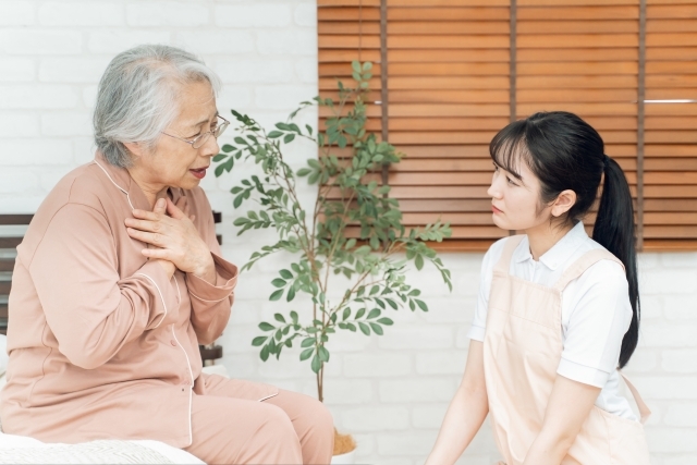 痛がる高齢者女性とエプロン姿の女性